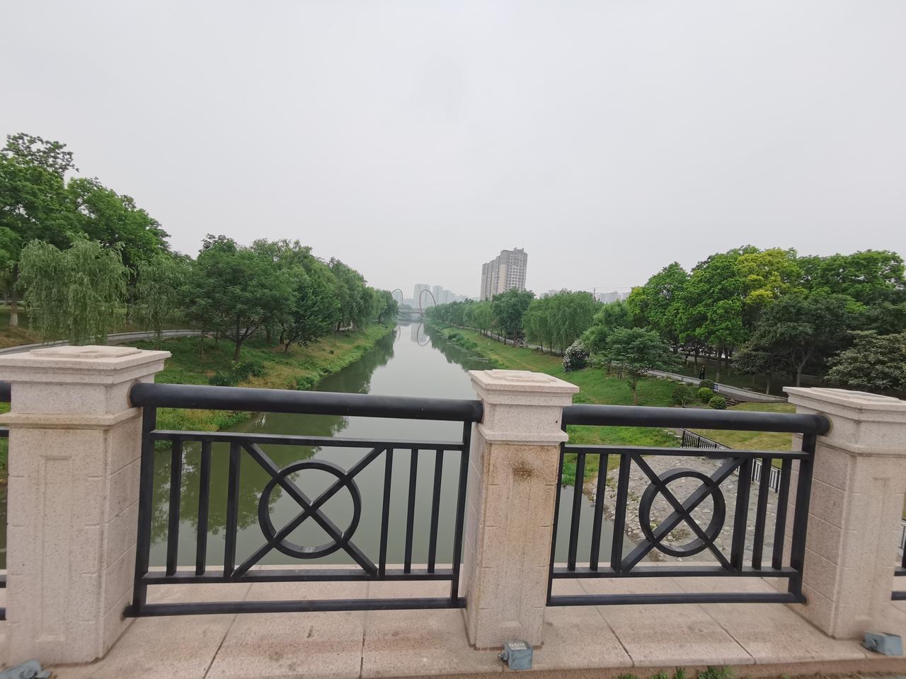 卫水河畔，
彩虹桥边，
长廊蜿蜒，
绿树掩映，
鲜花烂漫，
老人清闲散步，
对对