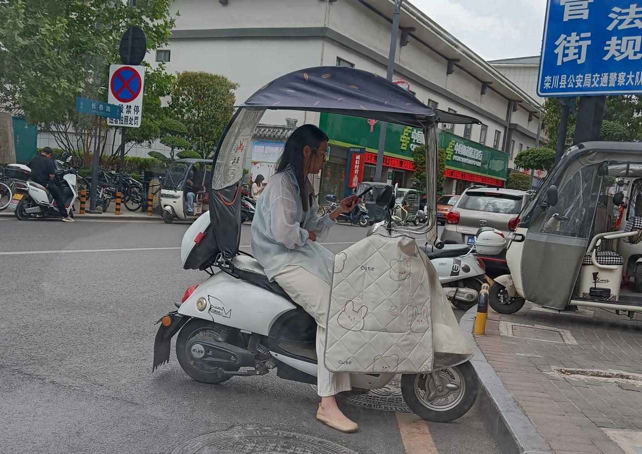 洛阳这边的小姐姐真有素质呀。街头骑小巧摩托车遇上了红灯，急忙停车在一旁，边瞧手机