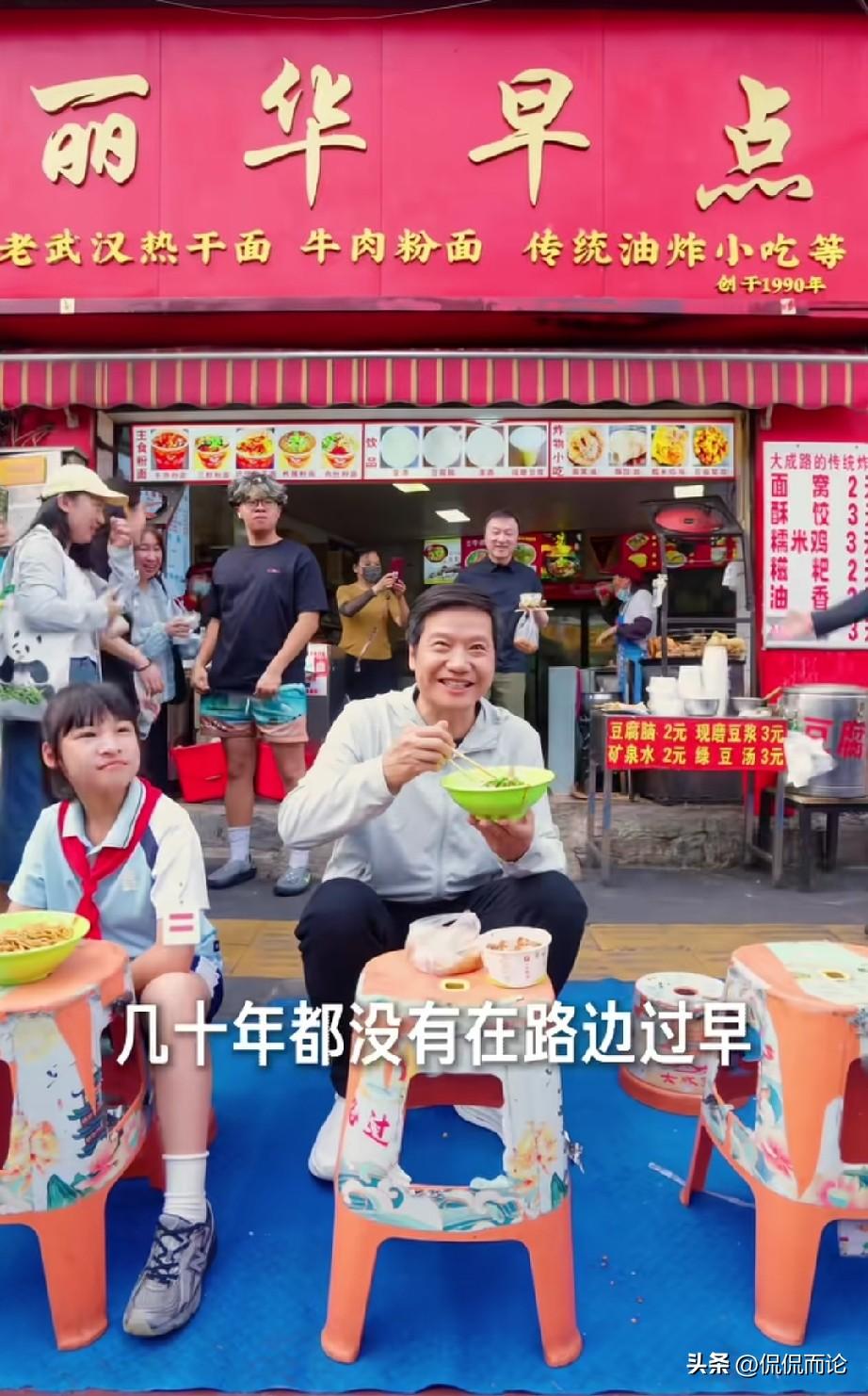 雷军非常接地气的在塑料小板凳上吃着早饭，早饭的三件套热干面、面窝、绿豆汤，旁边的