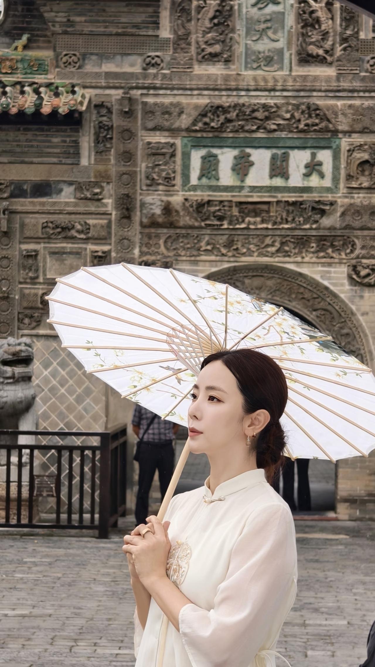 李思思身穿白色绣花纱裙，
手撑油纸伞，
站在花戏楼前，
古色古香，
韵味十足！