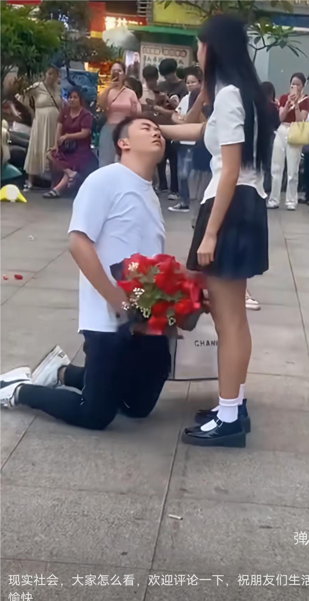 这样跪舔值得吗？
大街上一位穿白T恤的小伙子，一手拿着花，一手提着给女孩买的礼物