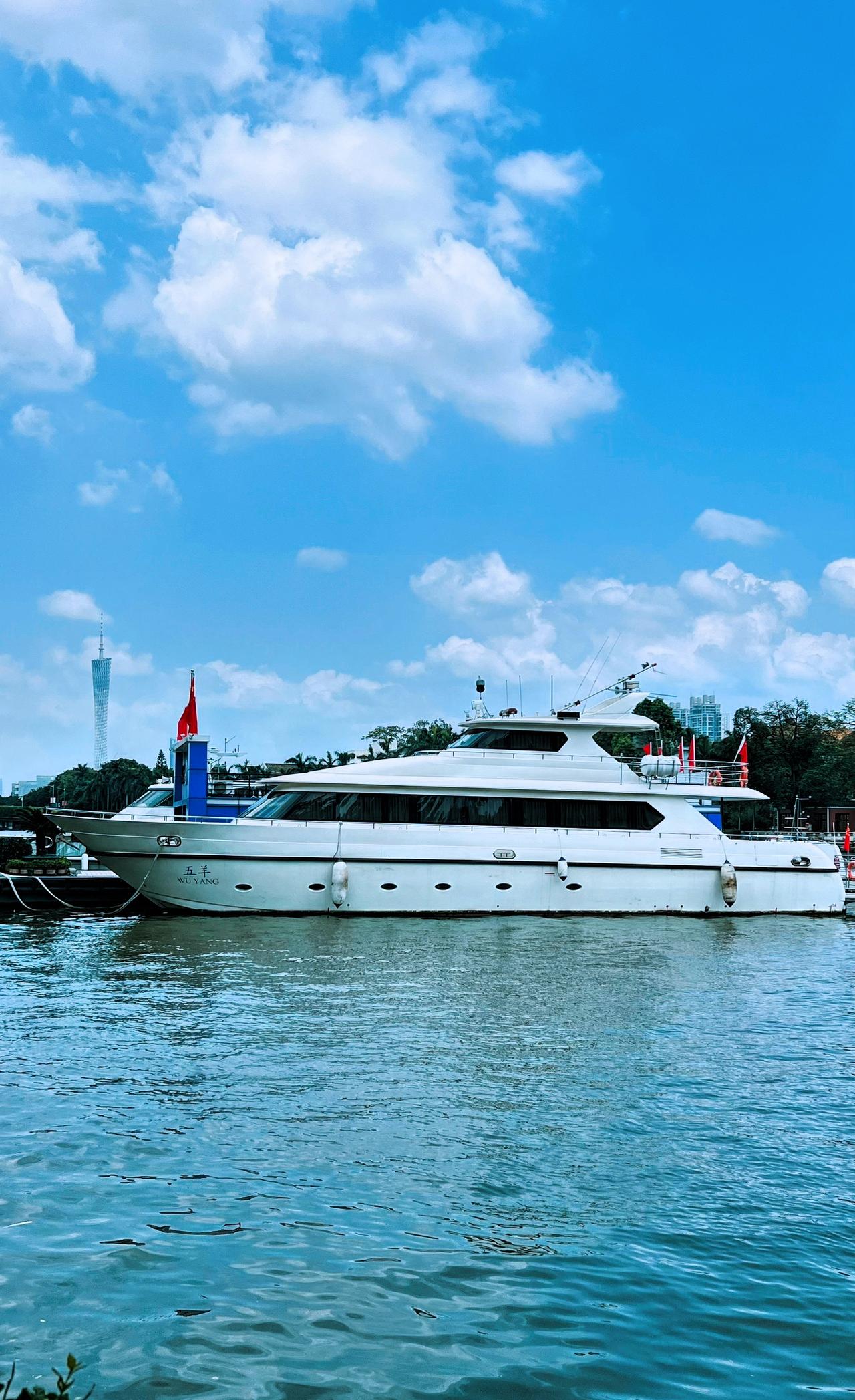 珠江风光：豪华游艇停泊在碧波荡漾的江面上，与蓝天白云相映成趣，尽显奢华与宁静。
