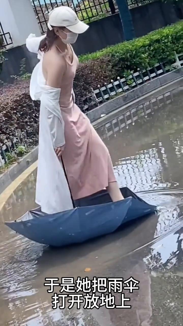 女子遇到积水路面，巧妙踩着雨伞过去了。
女子拿着雨伞正走时，突然她看到前面有一片