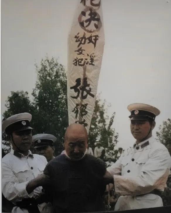 1983年，一名男子即将被执行死刑，他的头低垂，神情黯然，身后的牌子上白纸黑字，