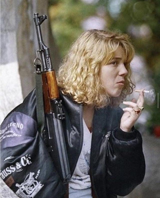 这张1992年萨拉热窝葬礼上的照片里，女孩手持AK-47抽着烟，档案只标注为“波