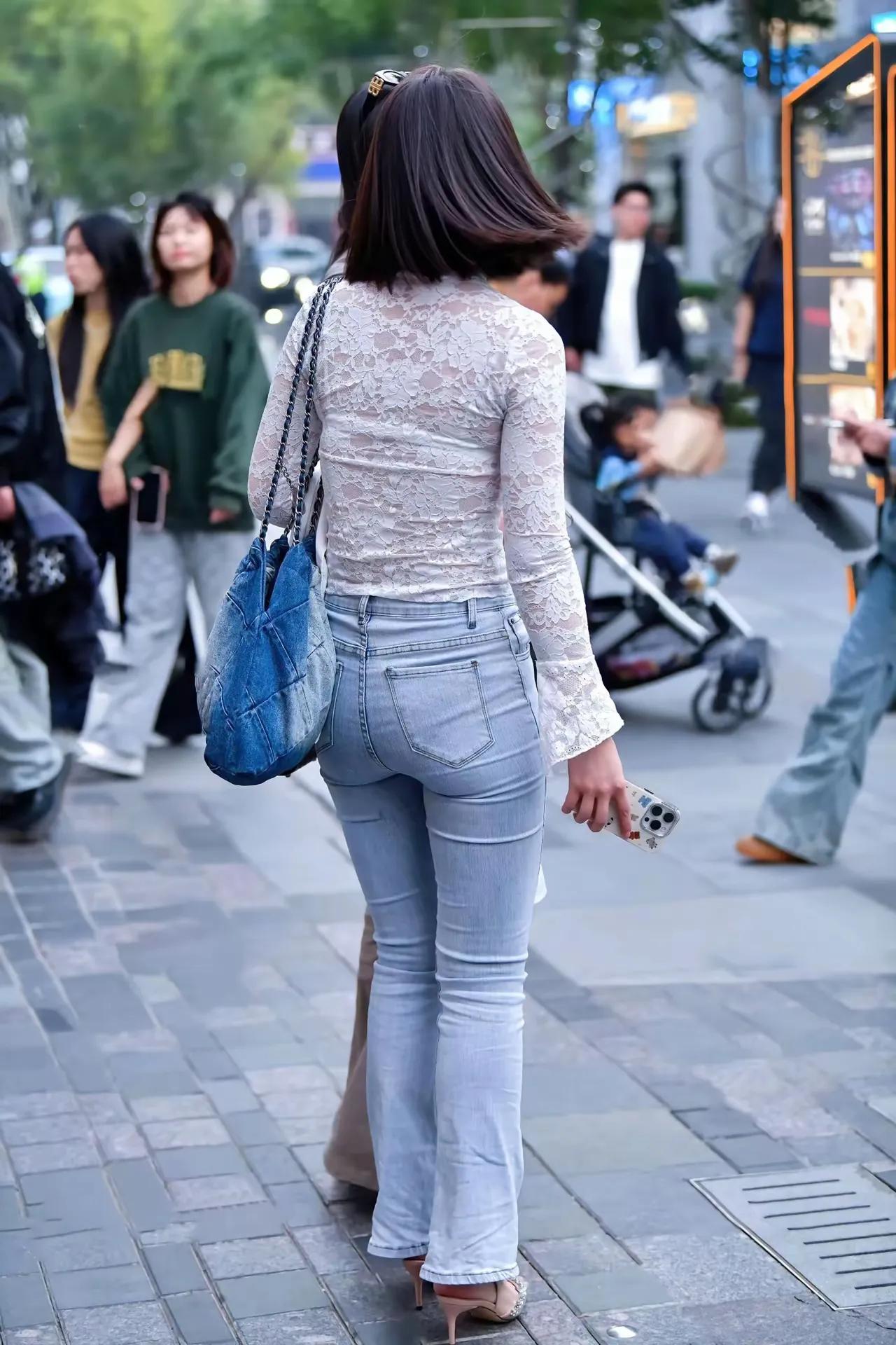 一个穿牛仔裤的女士在街上走着。经典牛仔裤要怎样搭配简约又时髦 白衬衫怎么穿搭出时