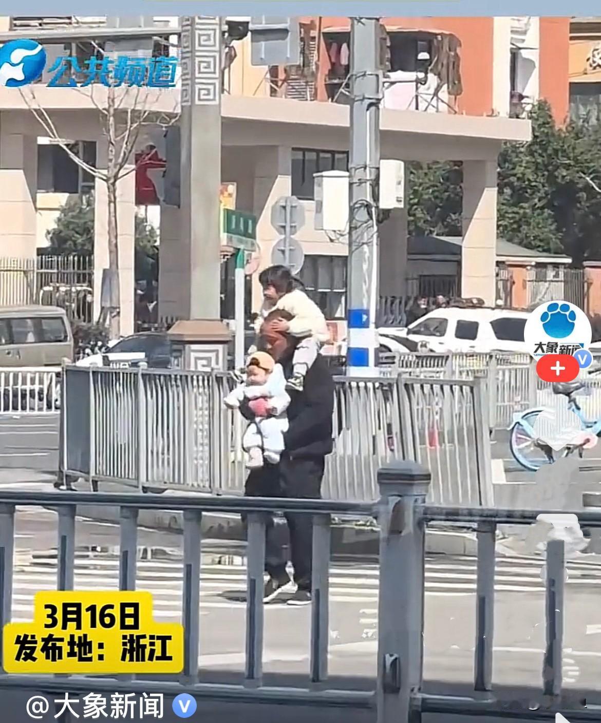 近日，浙江一车来车往的马路上，一爷爷手里抱着小孙子，肩上扛着小孙子在过马路，虽然
