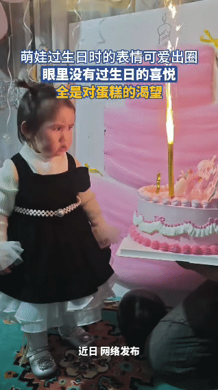 生日宴现场，身着黑白公主裙的萌娃站在装饰好的生日蛋糕旁。蛋糕上的烟花蜡烛正在燃烧