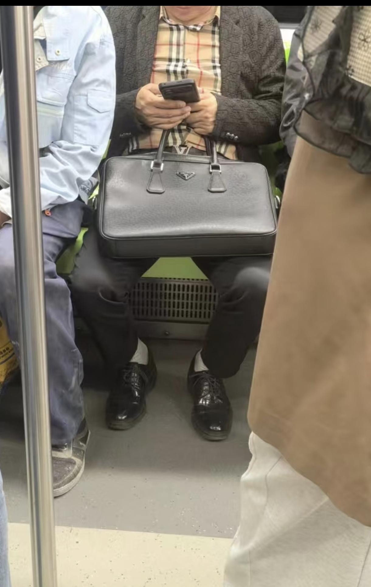 这位大哥衬衫像巴宝莉的，格子都没对齐，包包像普拉达长青款。黑皮鞋配白袜太掉价了，