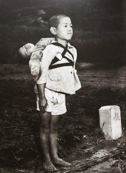 这张照片拍摄于1945年、已经被美军占领的日本某地。照片名为：站在火葬场旁的男孩