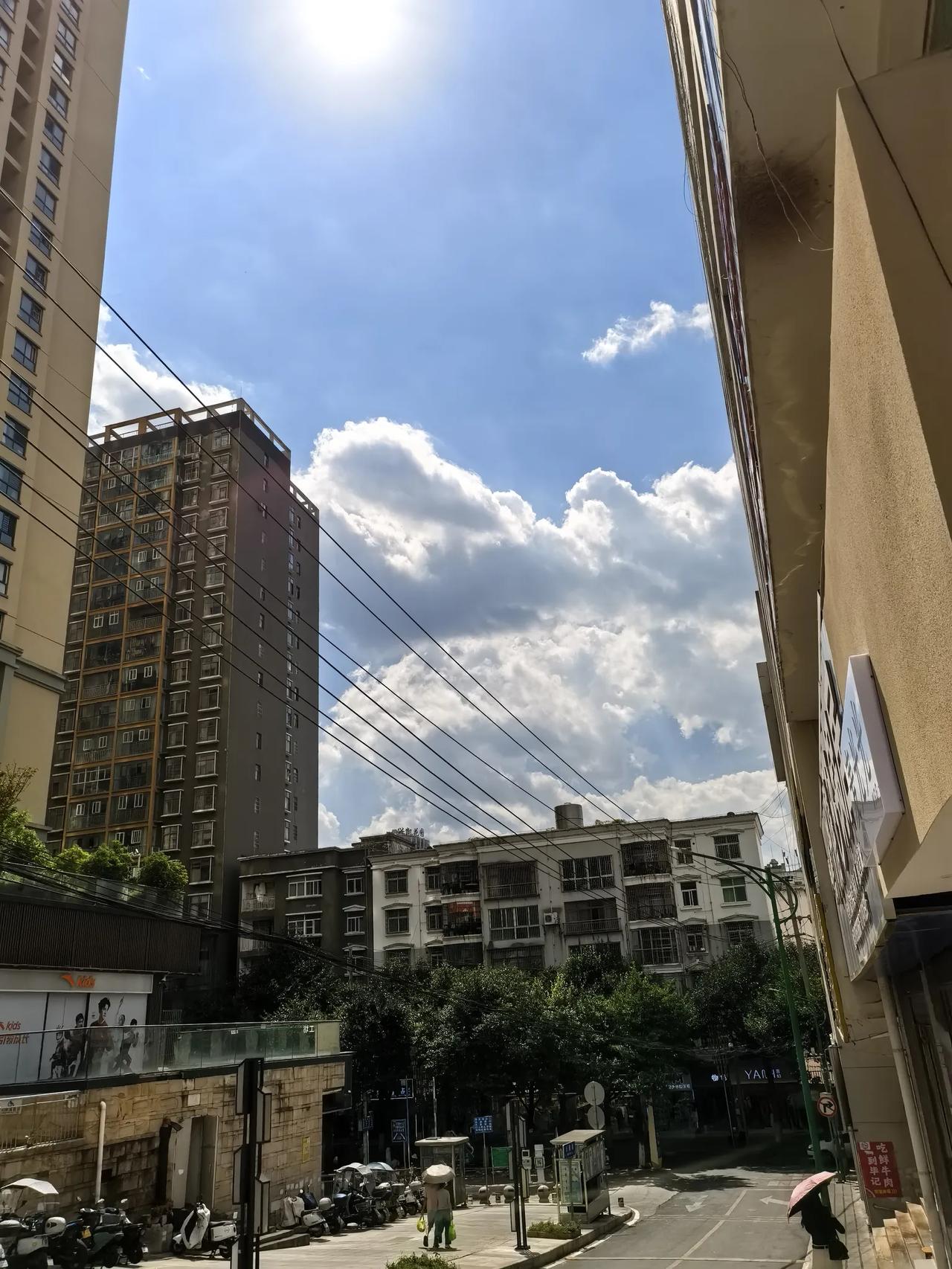 篮天白云下的城市建筑与人流如织的市民，悠闲漫步于街道两边，形成一道人间烟火气十足