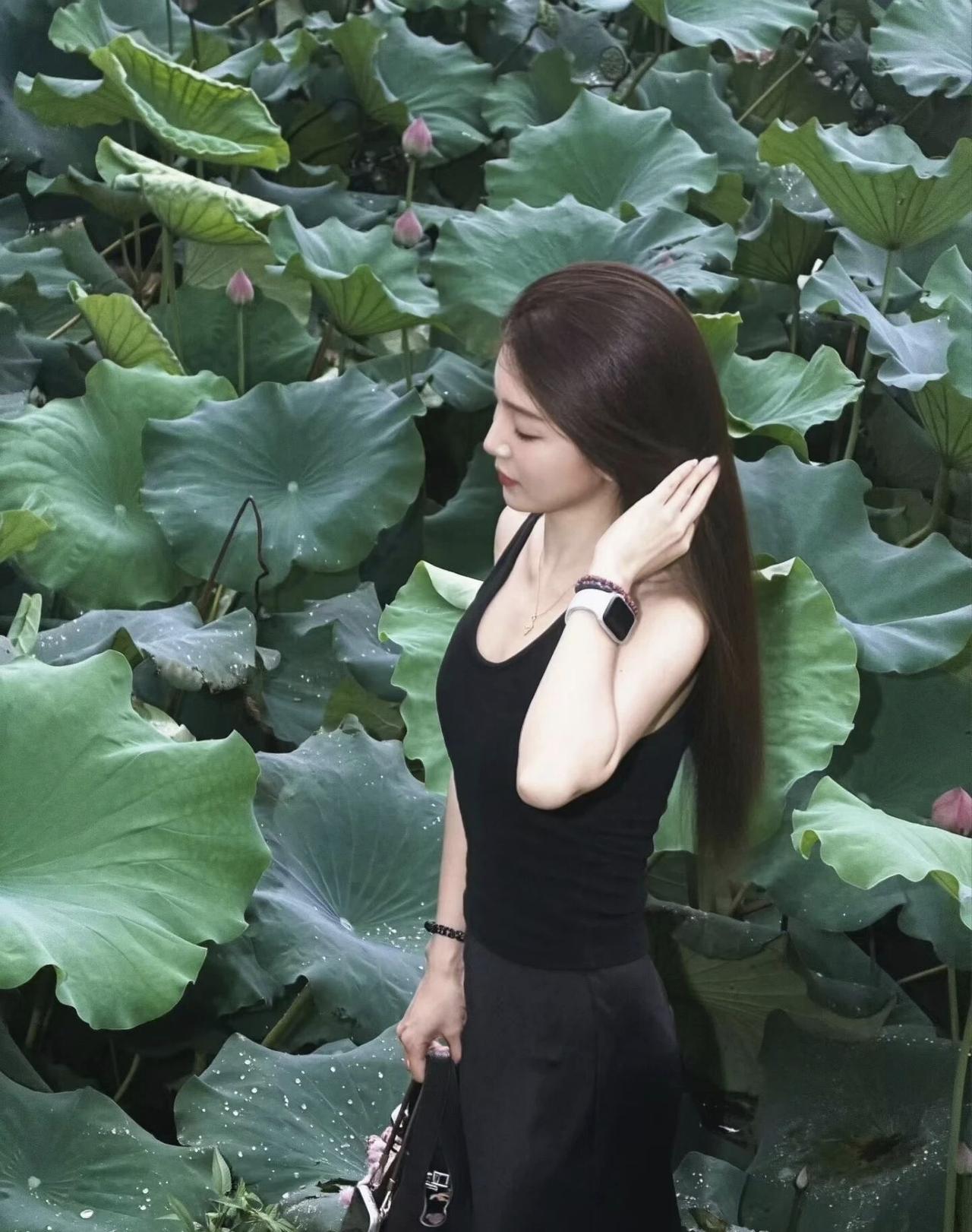 一位女士站在荷叶丛中，显得很优雅。