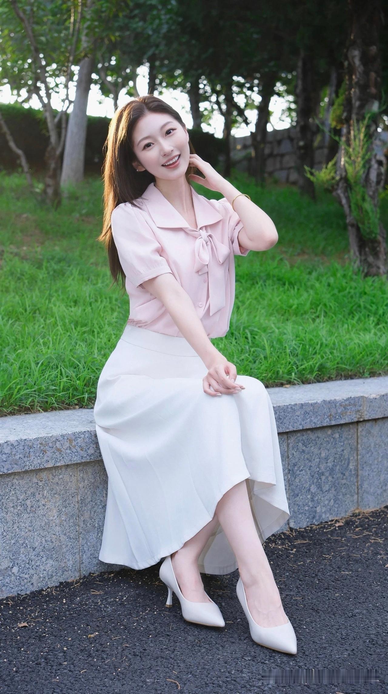 这位女士坐在公园的石墙上，微笑着看向镜头。
