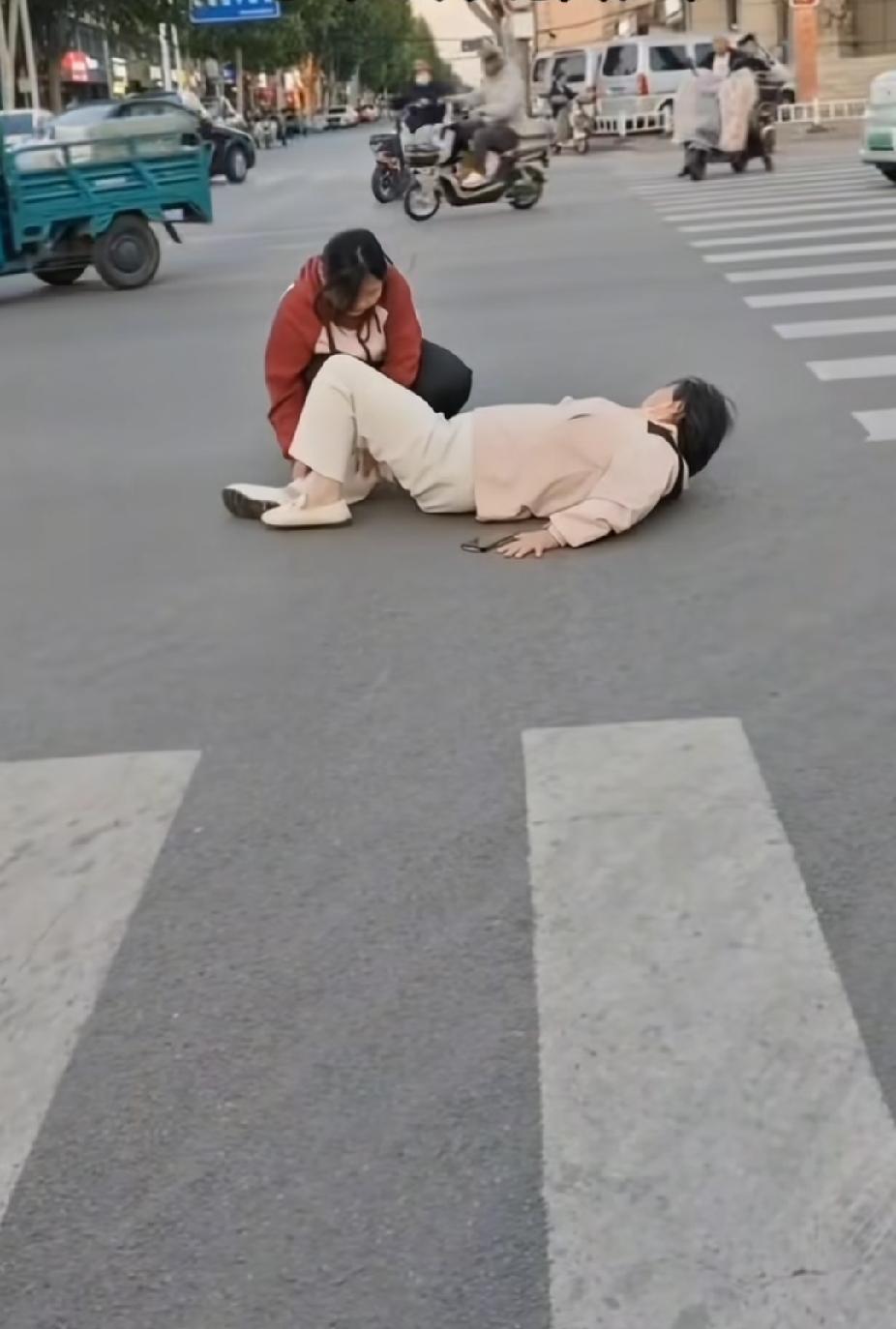 一名女子躺在马路上，路人皆从女子身旁匆匆而过，一位小姑娘的出现，让人看着感动了。