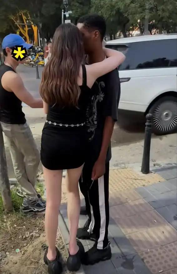 一黑人男子搂着一名年轻女子。只见这名女子站在原地一动不动，把头埋在男子怀中，一开