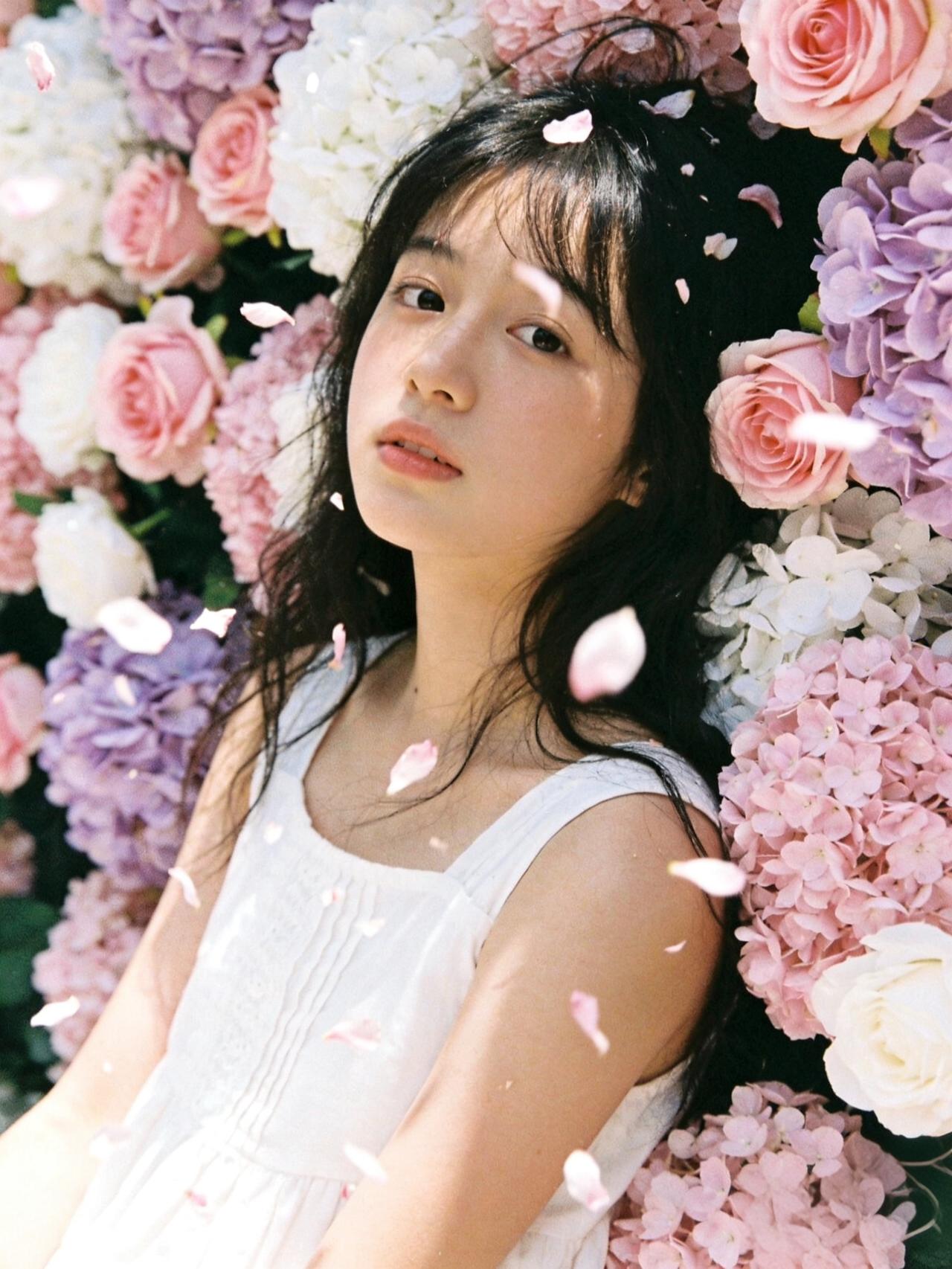 少女靠在花墙前，花瓣在空中飘落。