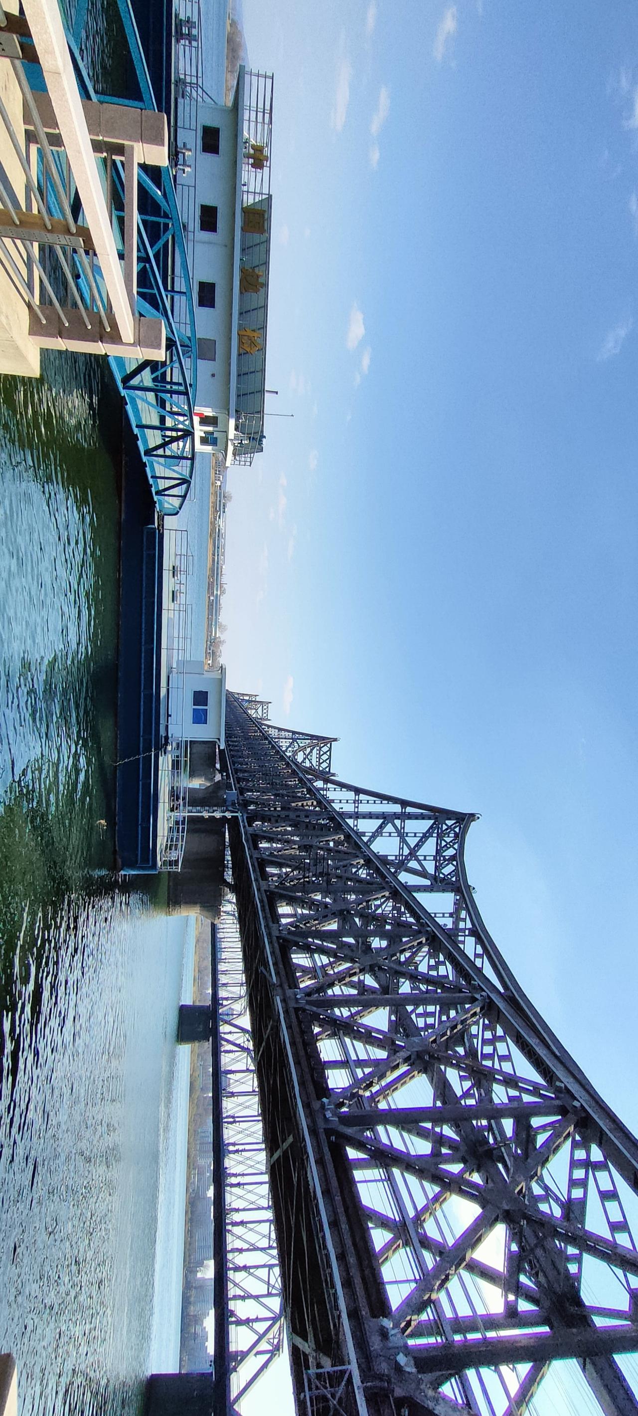 工业风铁桥，俯瞰水面，蓝天白云，宁静而壮观。