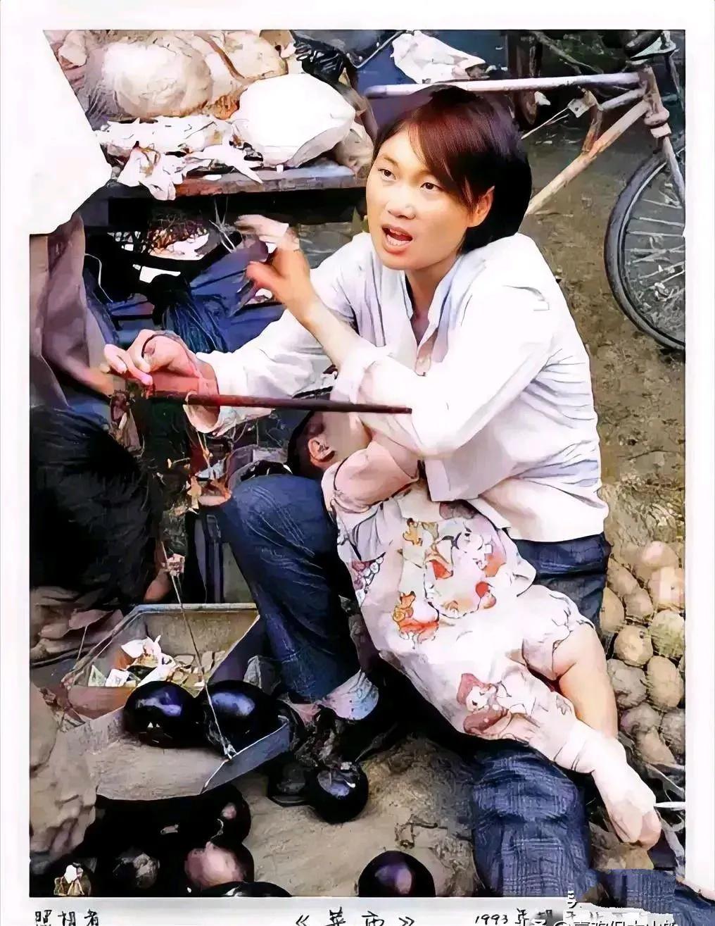 1993年，北京菜市，一名年轻母亲带幼儿卖菜的照片

照片中，这名母亲一边给客人