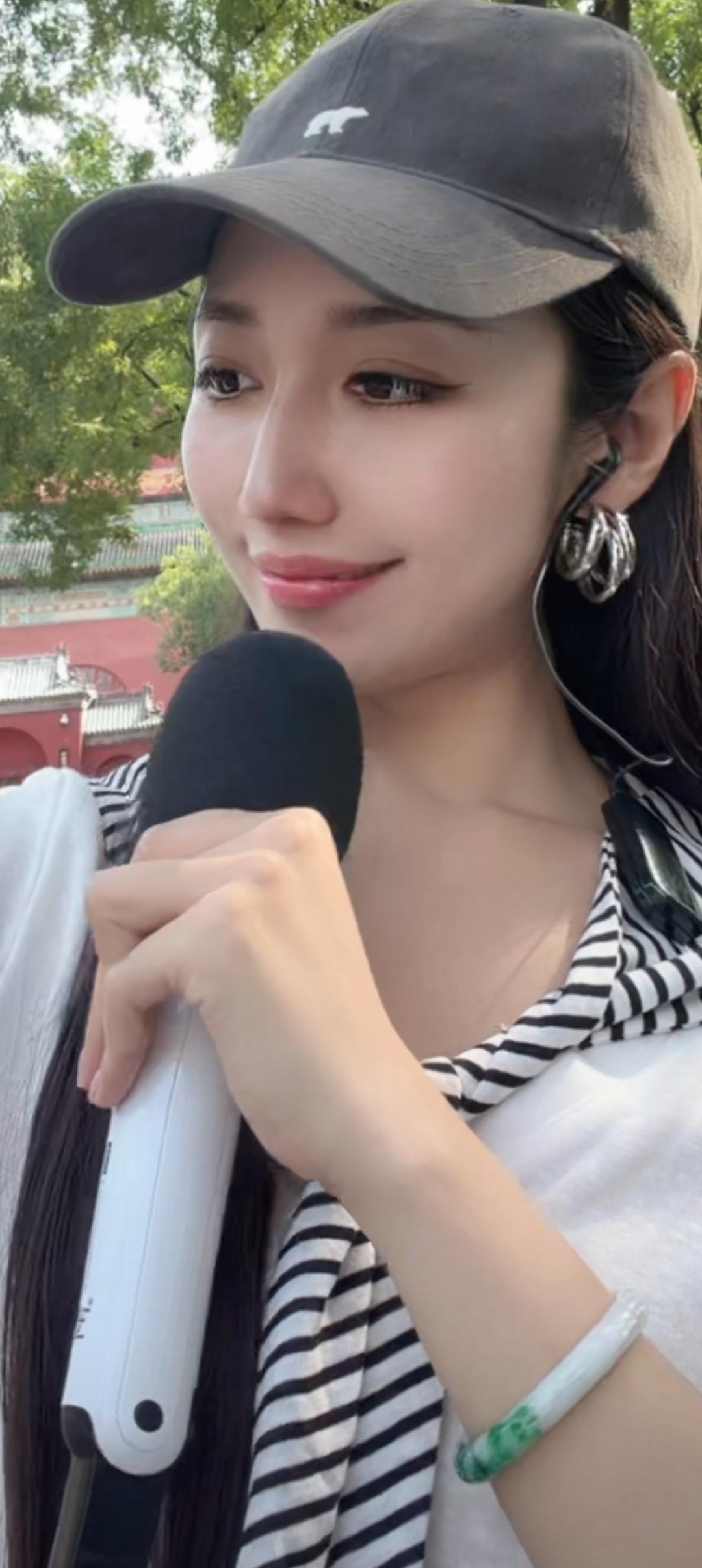 戴着帽子，拿着麦克风，笑容甜美。