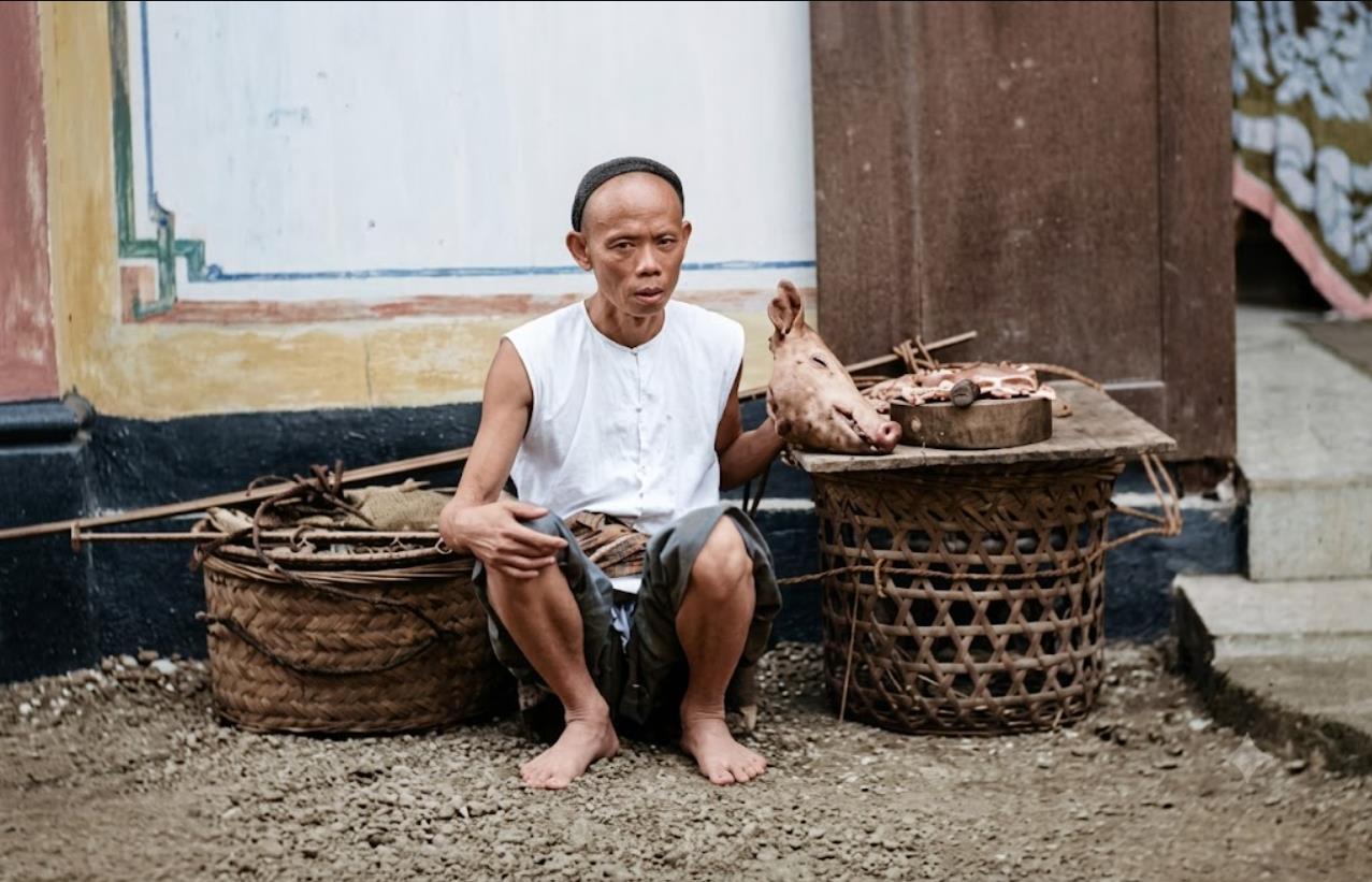 清末街头，流动肉食小贩蹲守待客，小贩身形清瘦，头裹简易布巾，身着无袖短坎肩与短裤