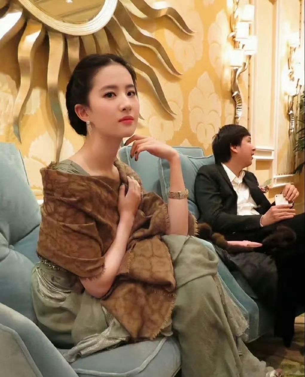 刘亦菲这次内搭灰绿色丝质长裙，面料垂坠光泽感十足，低圆领设计尽显温婉。外搭棕色提