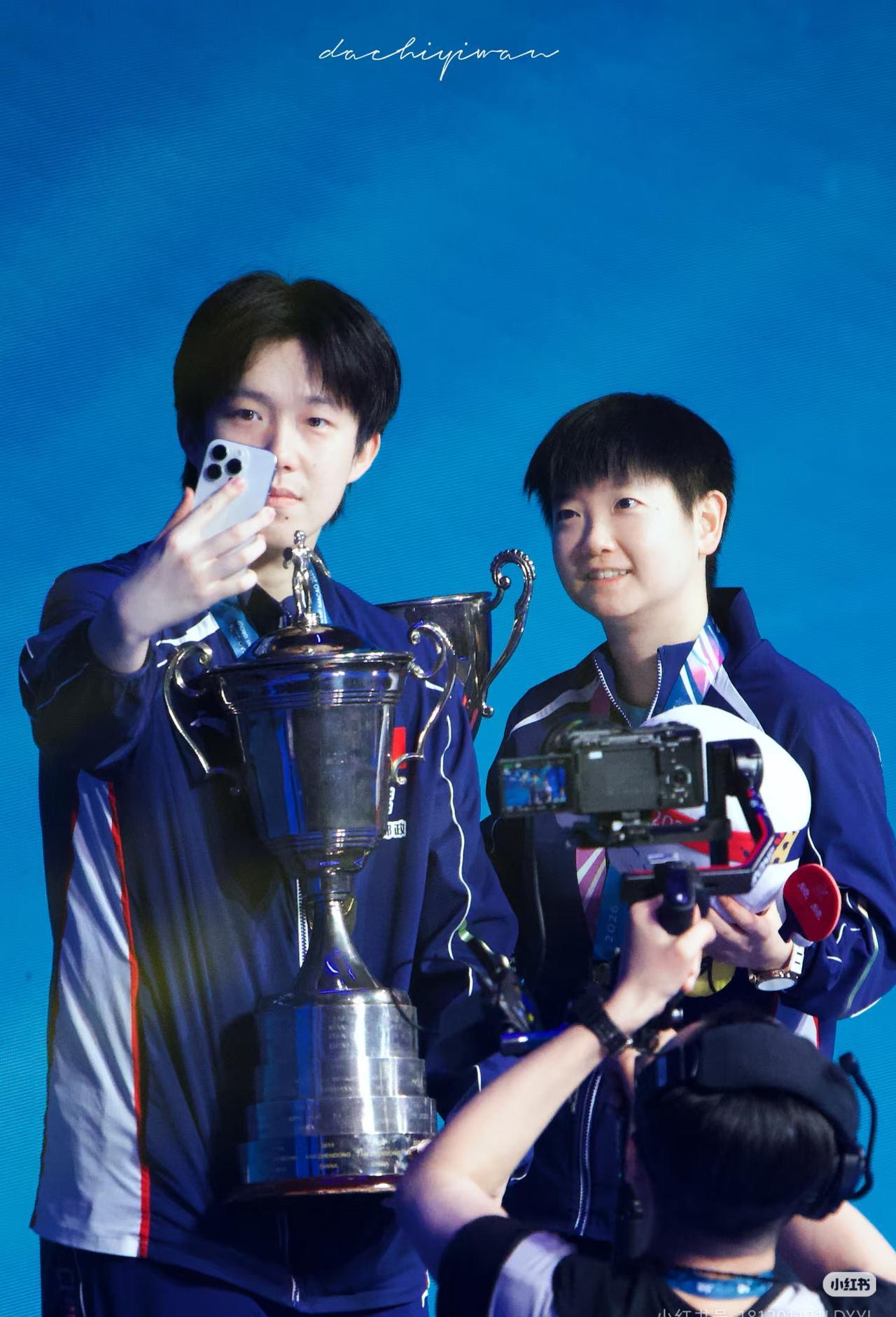 孙颖莎凌晨4点拖着箱子，箱子外挂着一条没拆吊牌的粉色新裤子。
网友看到照片，说