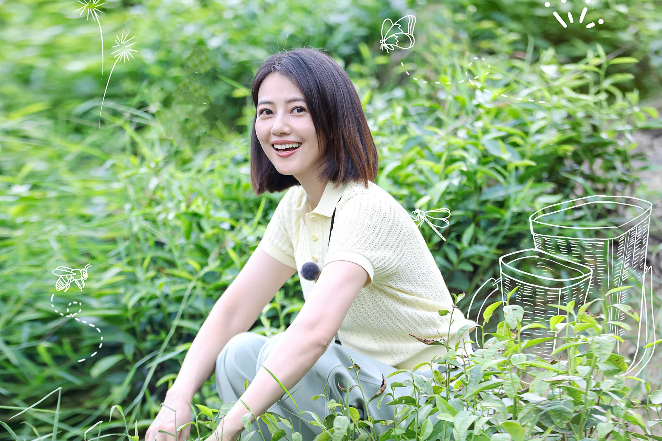 一片清新的绿意中，浅黄针织衫与浅灰裤装的搭配，让她整个人显得温柔又松弛。她的笑容