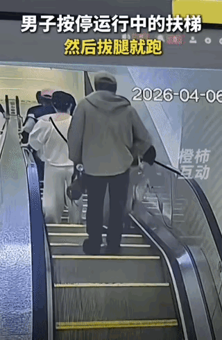 众多顾客乘坐滚梯下楼，此时一位男士跑过来，迅速按下扶手下面的停车按钮后溜了，差点