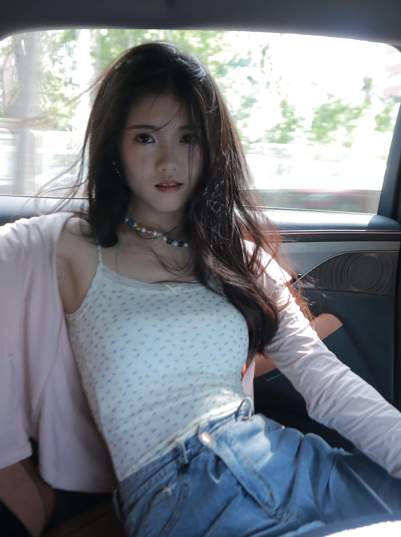 穿着带有波点的白色吊带、浅粉色开衫和蓝色牛仔裤，佩戴着彩色串珠项链，而头发自然垂