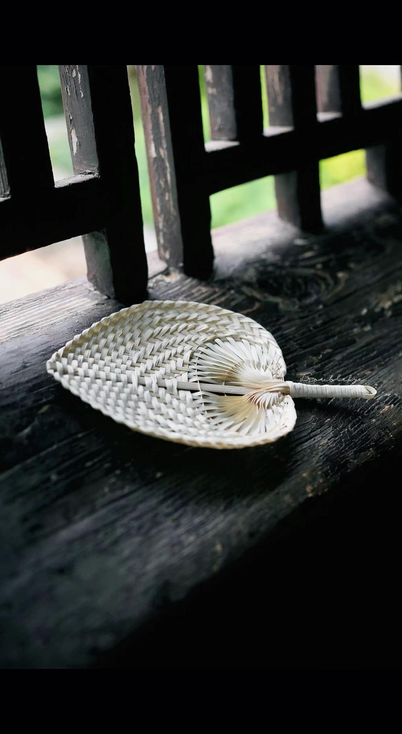 🪑竹编扇躺在老木上，像片凝固的云☁️。风过时，纹路里藏着整个夏天的蝉鸣🌿。慢