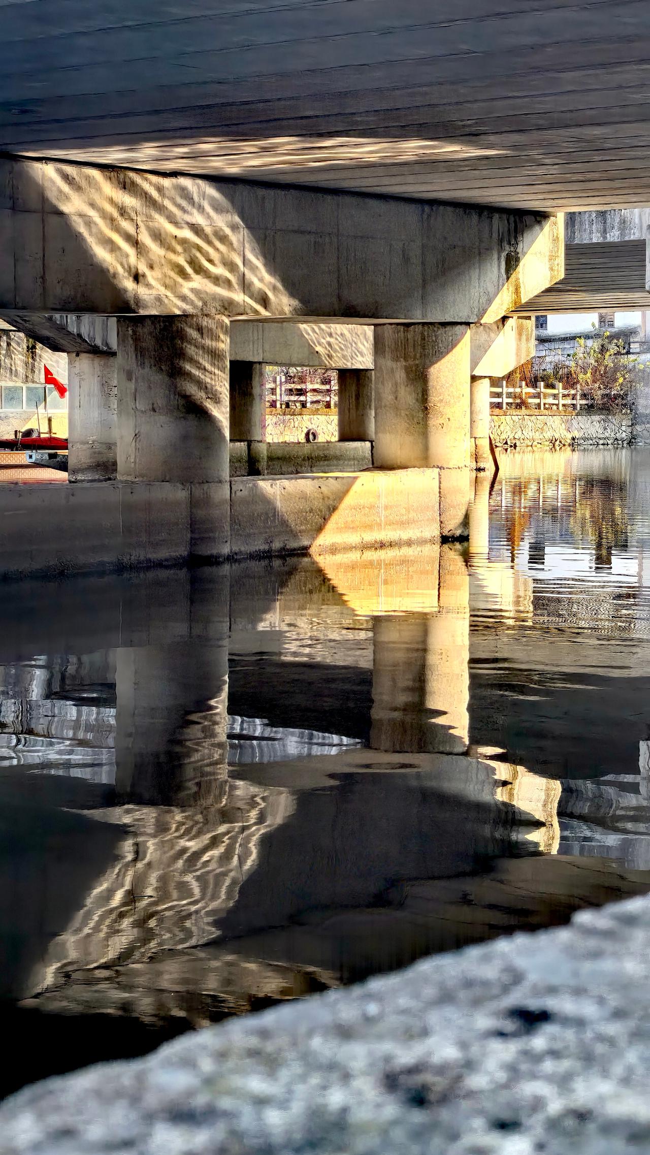 夕阳照射桥墩，又在倒影下反射情形，形成三角、线条、框图、黑白等各种叠透立面光影