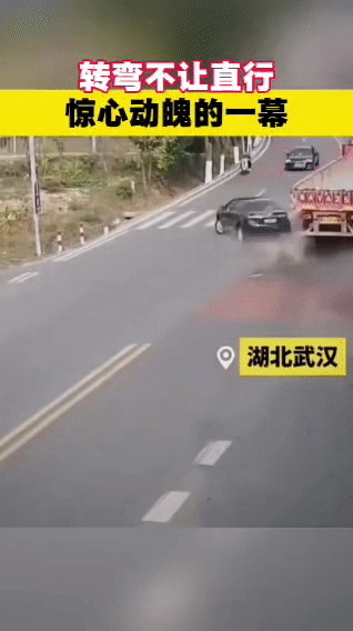在湖北的一段道路上，一辆黑色轿车在转弯时未避让直行的红色大货车。大货车虽紧急处置