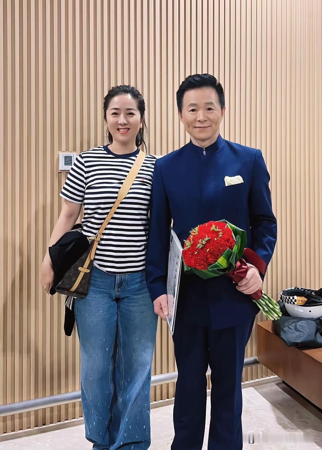 王宏伟手拿着鲜花，整个人显得比较年轻有气质，58岁了头发还那么的乌黑，他人品好，