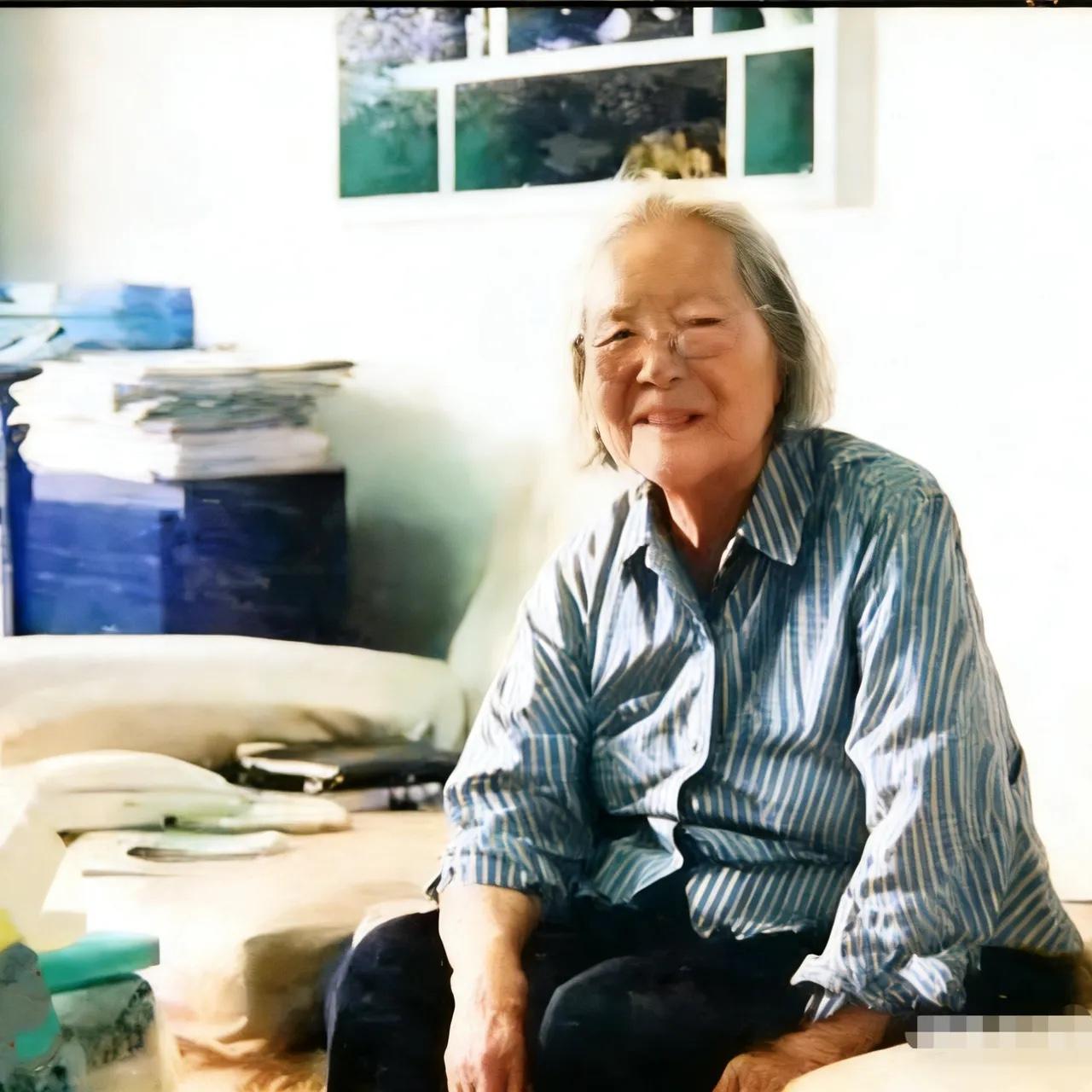 2003年，退休多年的傅冬菊老人坐在沙发上的照片，家里十分朴素，她对着镜头微笑，