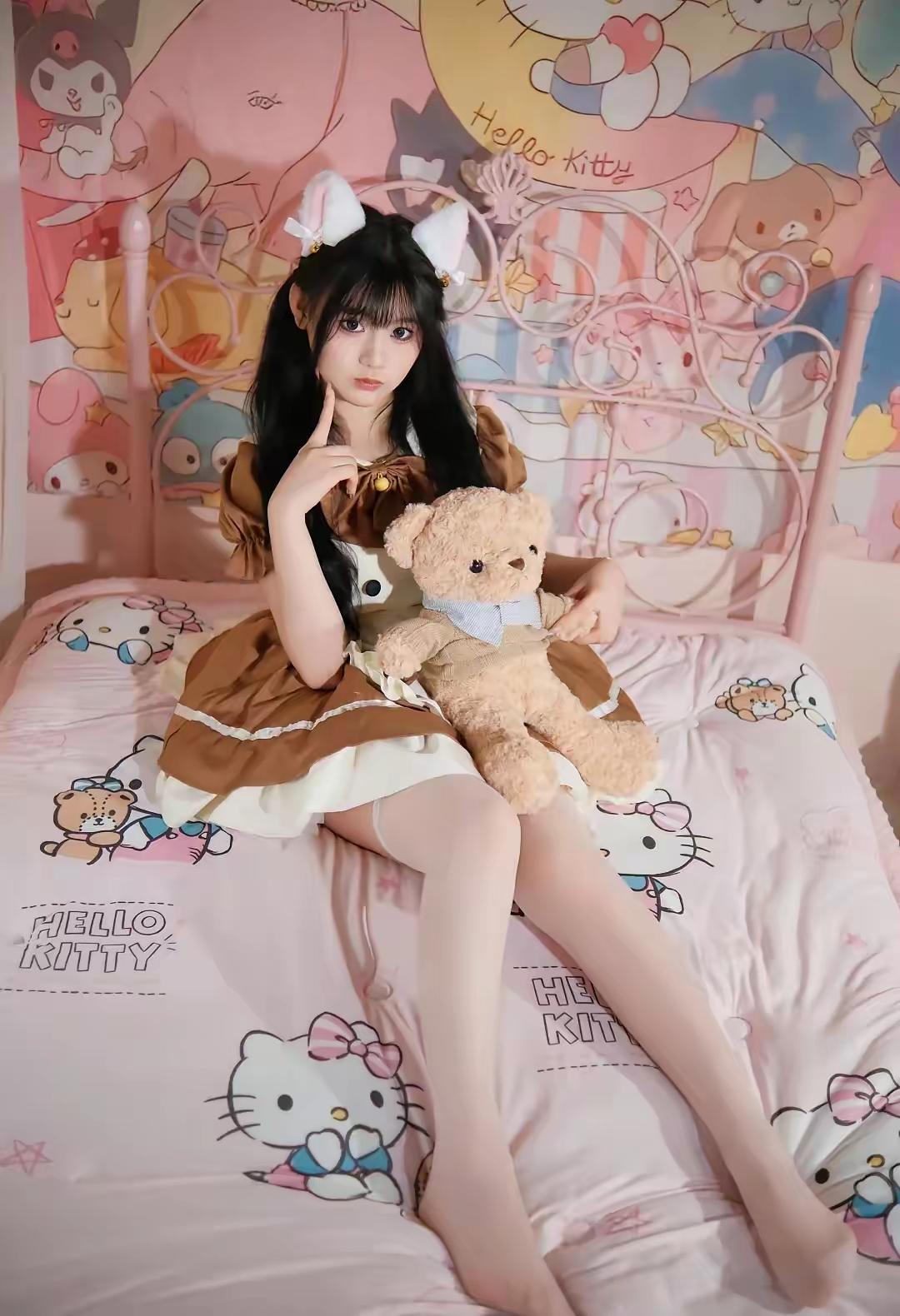 这女孩穿着可爱服装坐在床上，抱着Hello Kitty玩偶。