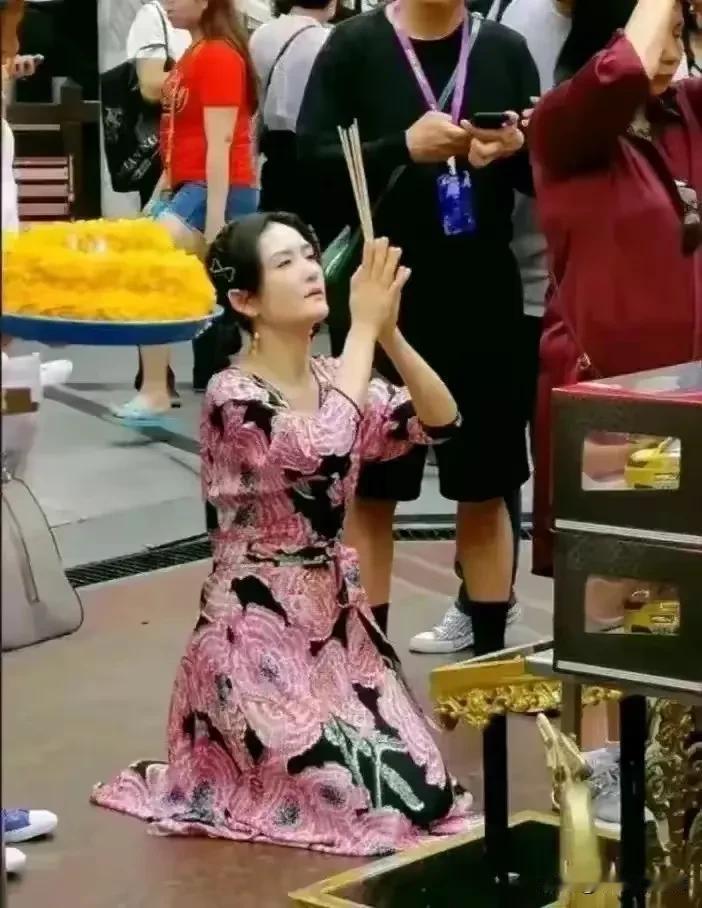 照片中这个女人虔诚的跪在地上，手里握着香，态度非常的端正，希望她的祈求能够得偿所
