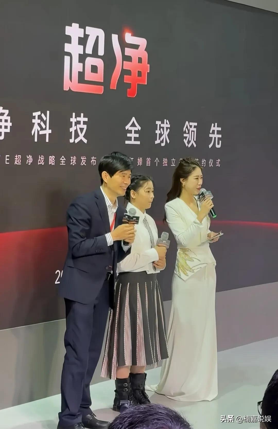 全红婵出席她的首个独立代言产品签约仪式。
她盘着精致的发型，穿着一件白色的衬衫配