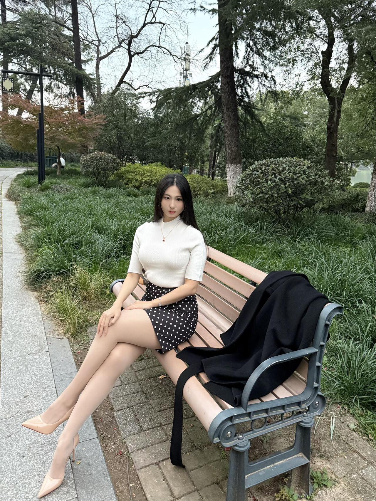 在公园的长椅上，她静静地坐着，仿佛与周围的自然融为一体。她的穿着简单而不失优雅，