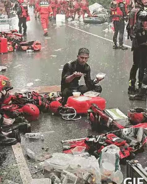 广西贵港，消防战士救援间隙坐地吃盒饭，雨来得像突然开闸。大雨劈头盖脸砸进饭盒，菜