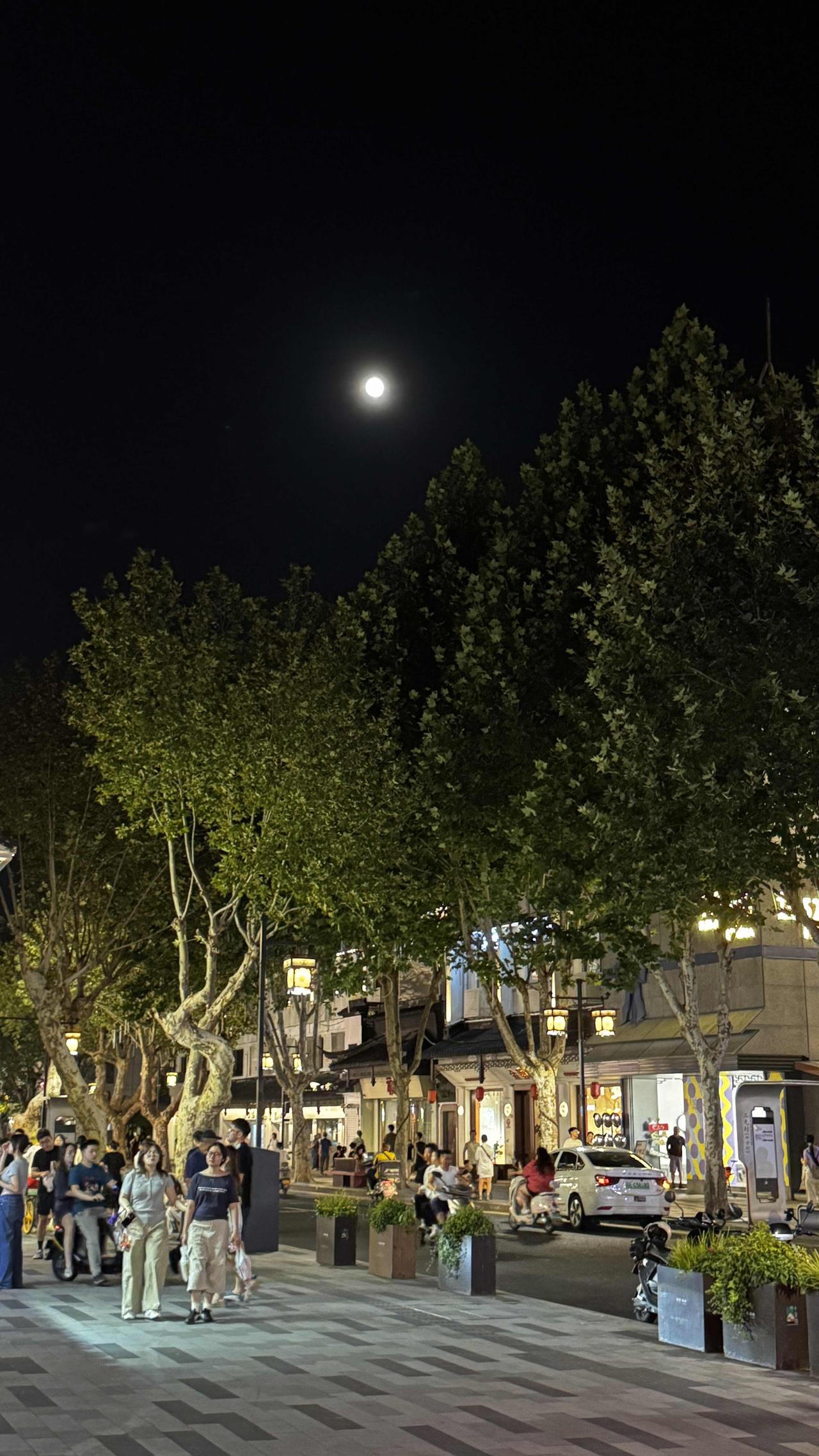 夜幕下的城市烟火气市井街巷灯火璀璨，行人往来熙熙攘攘。一轮明月悬于夜空，把温柔月