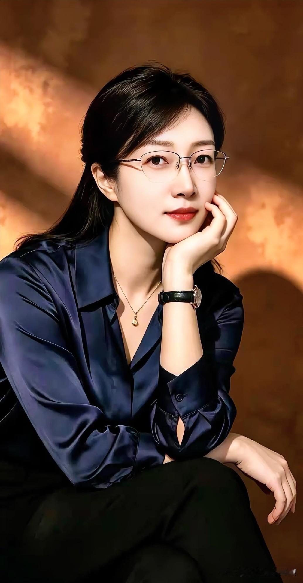 暗调暖光织就静谧，深蓝丝缎晕染知性。纤指托腮，眸藏星河，腕间表盘静默，她以从容姿