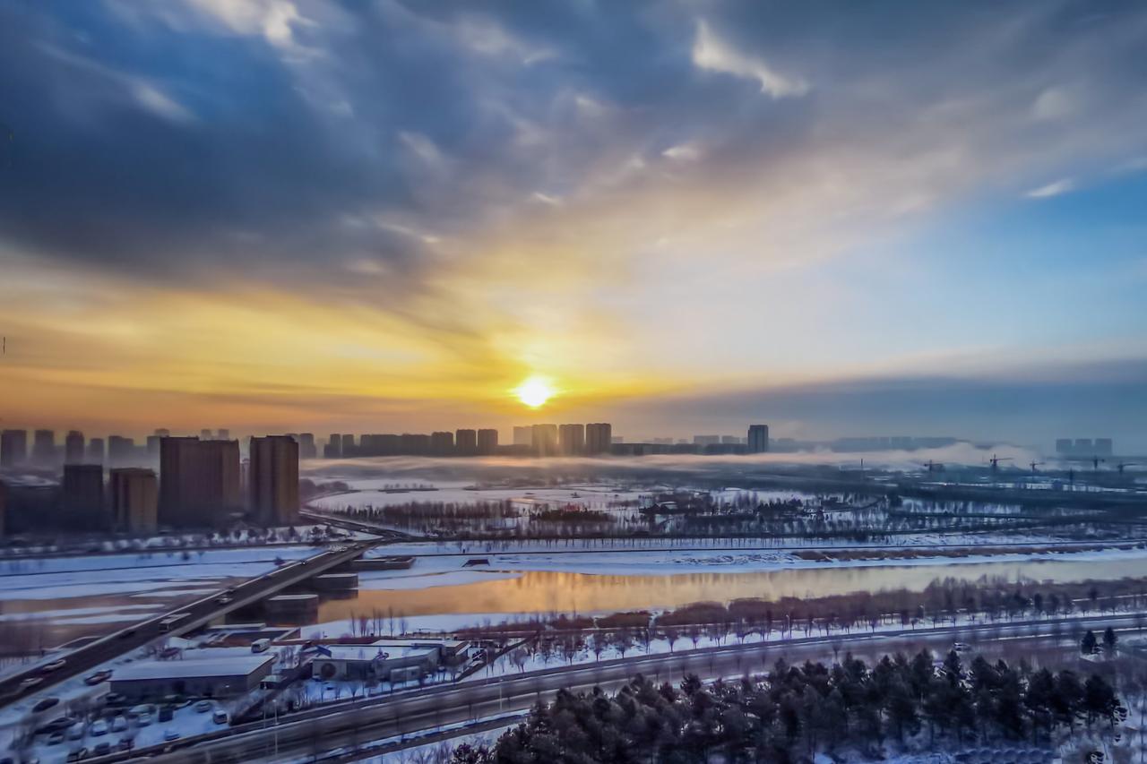 伊通河把冬日的晨昏酿成了温柔的诗。
清晨时，薄雾轻笼着雪色河岸，朝阳挣破灰蓝的云