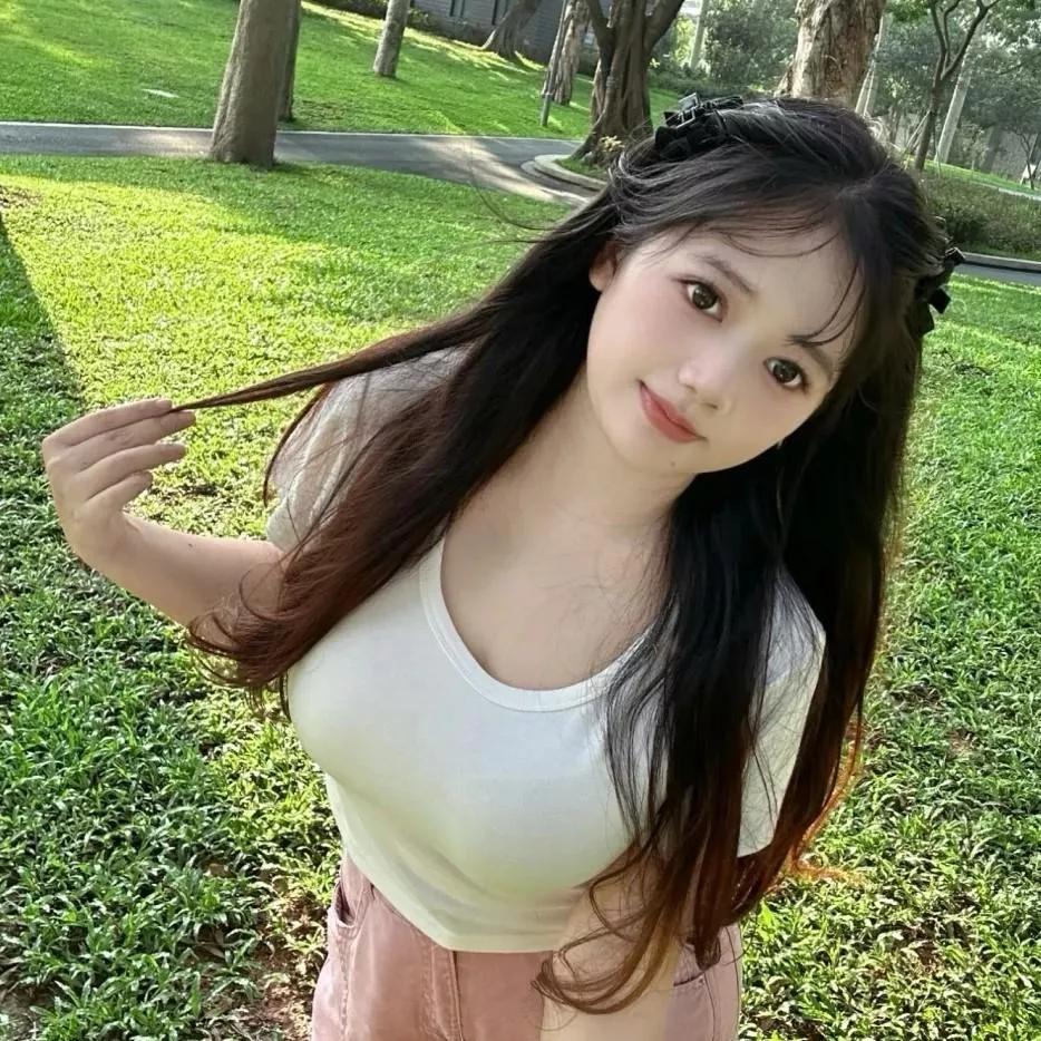 在阳光明媚的公园里，微笑的少女轻轻拨弄着长发，享受着自然的美好。