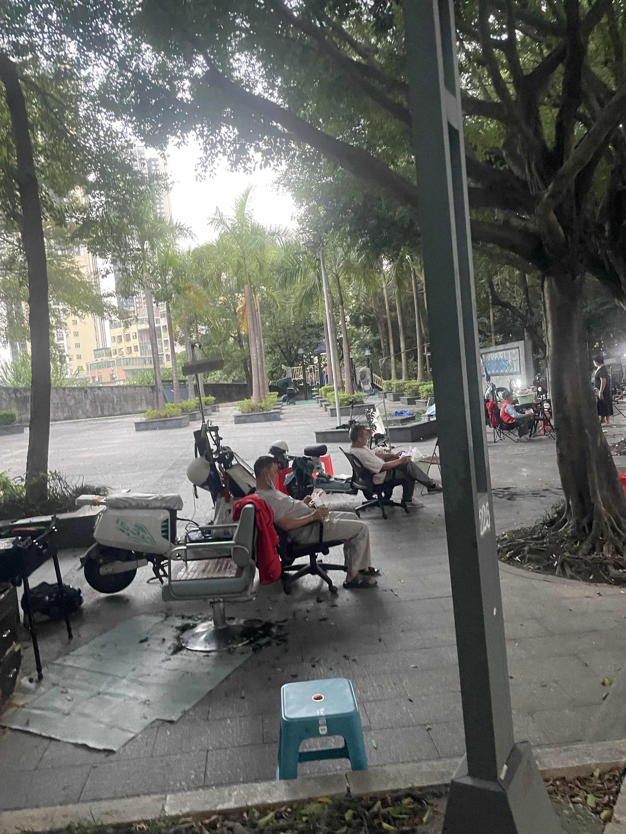 理发10元一个人！这是深圳的价格！都变了理发一条街了！几个老人在树下聊天休息。