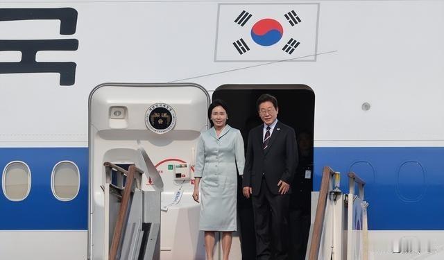 李在明总统携夫人走下专机舷梯，二人同框画面十分和谐般配。夫人一身浅灰色套装简约大