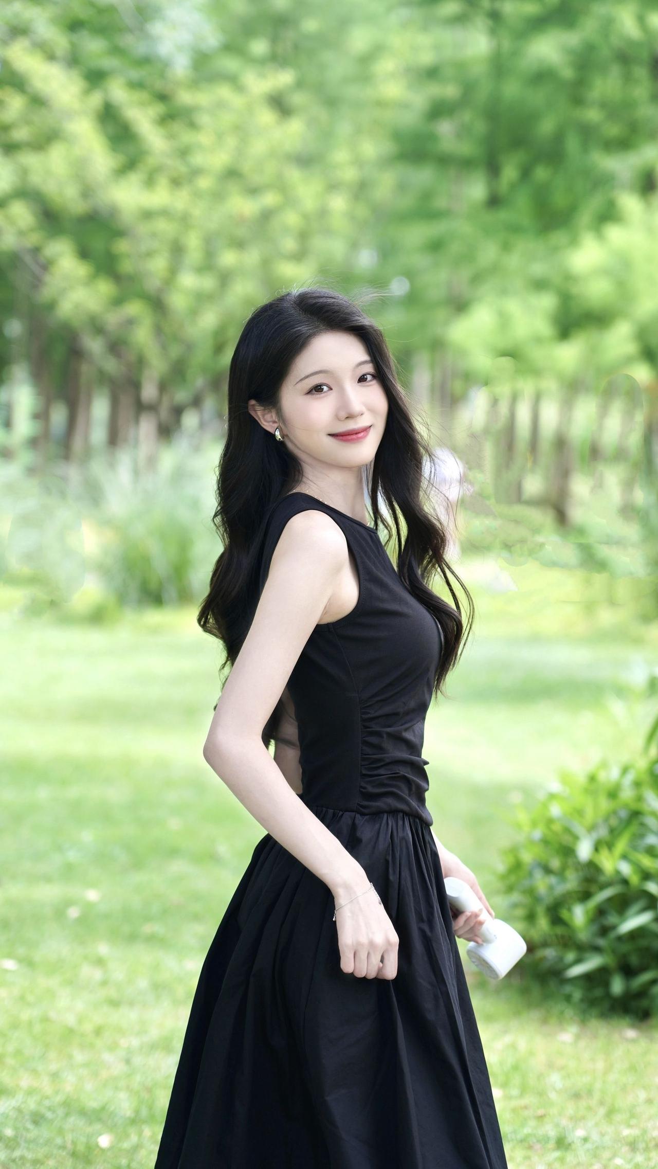 女人真正的气质是什么？林间绿意漫上来，一身沉静黑裙撞碎满屏清新。手持小风扇接住夏
