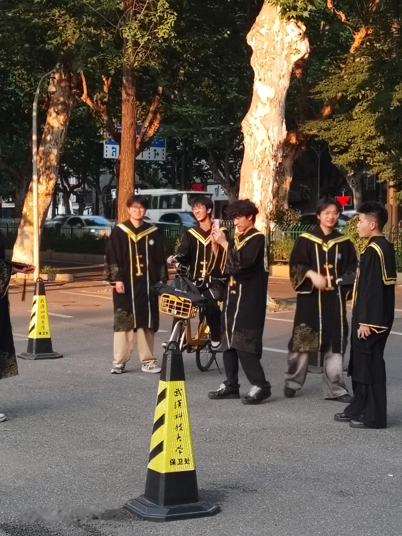 即将毕业的大学生穿着博士服，戴着博士帽在母校大门口留下美好的纪念。
  临近大学