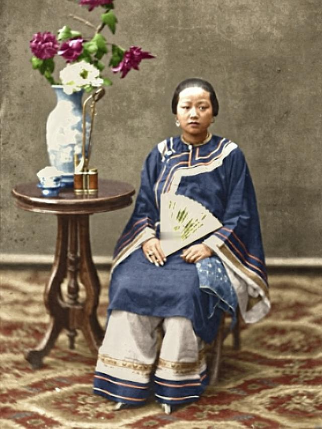 这是一张定格1880年广州大户人家女性的肖像，画面中的女子身着清代岭南服饰，斜襟