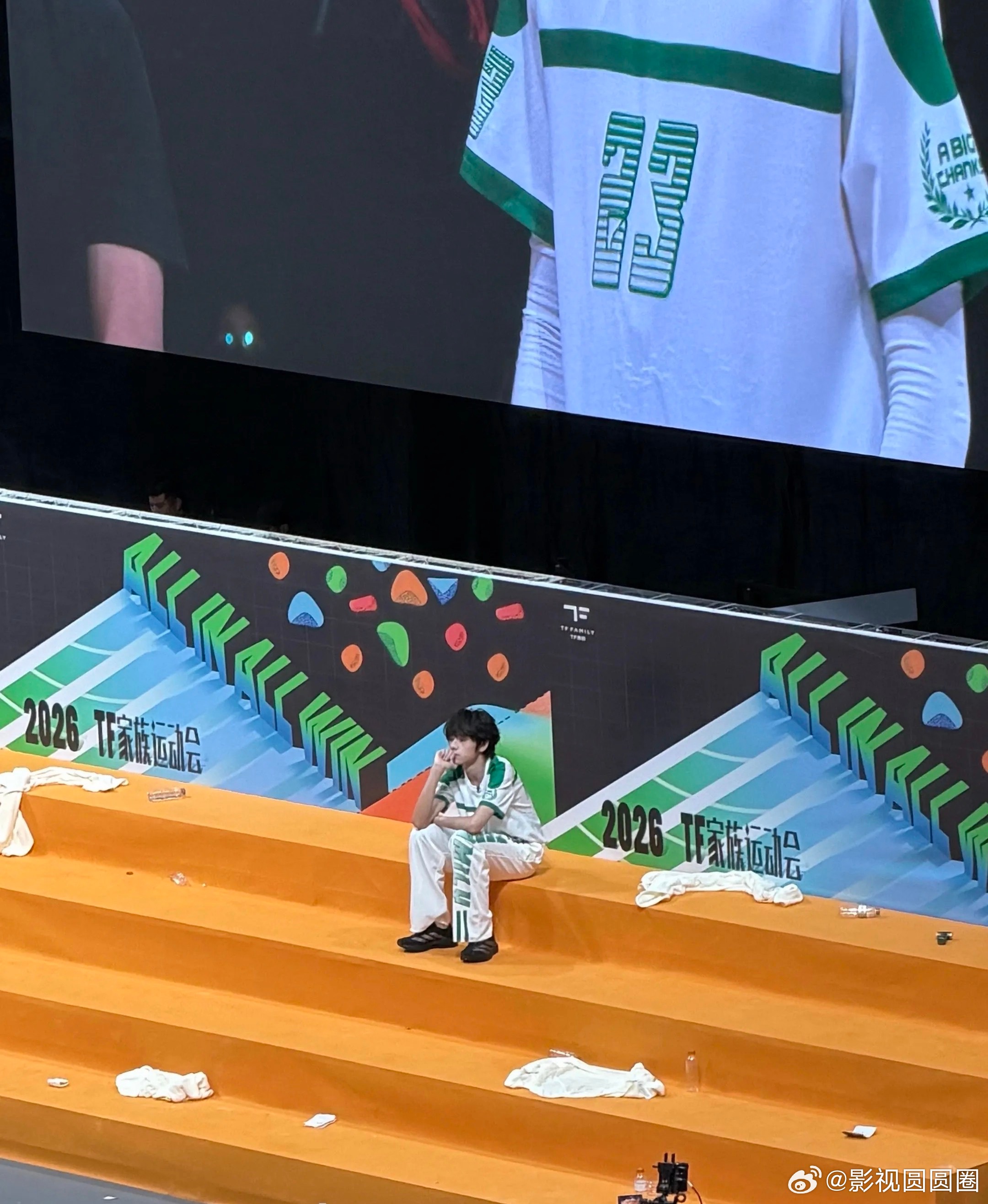 王橹杰运动会一个人坐着满场少年结伴互动玩耍，运动会热闹非凡，王橹杰单独静坐原地，