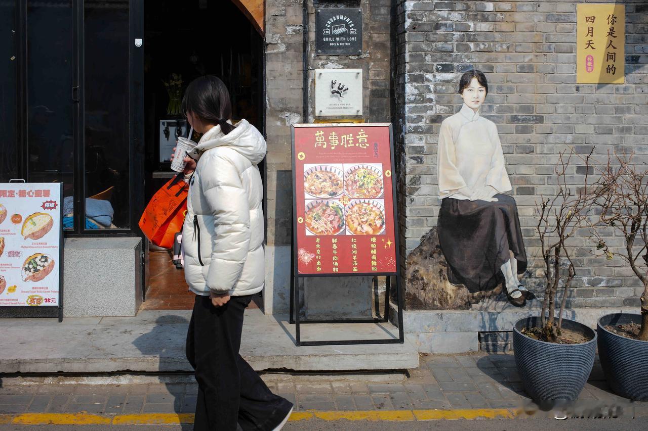 北京五道营胡同的暖阳里，老砖墙上静坐着民国风的墙绘，行人裹着冬衣走过，手里的热饮